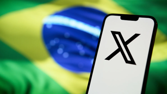 Smartphone displaying "X" logo in front of Brazilian flag.