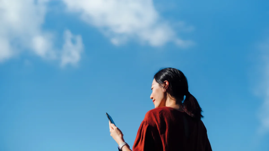 Woman looking at smartphone against blue sky.